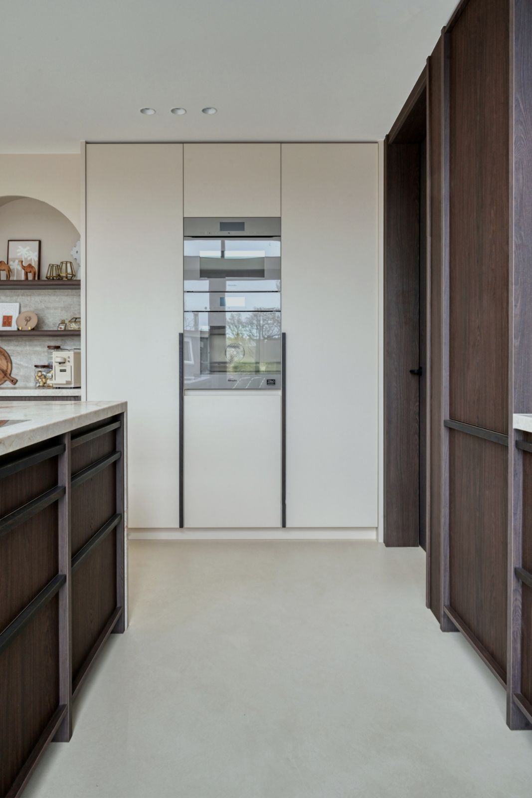 Badkamer met een warme beige gietvloer en wand, houten badmeubel en koperen kraan