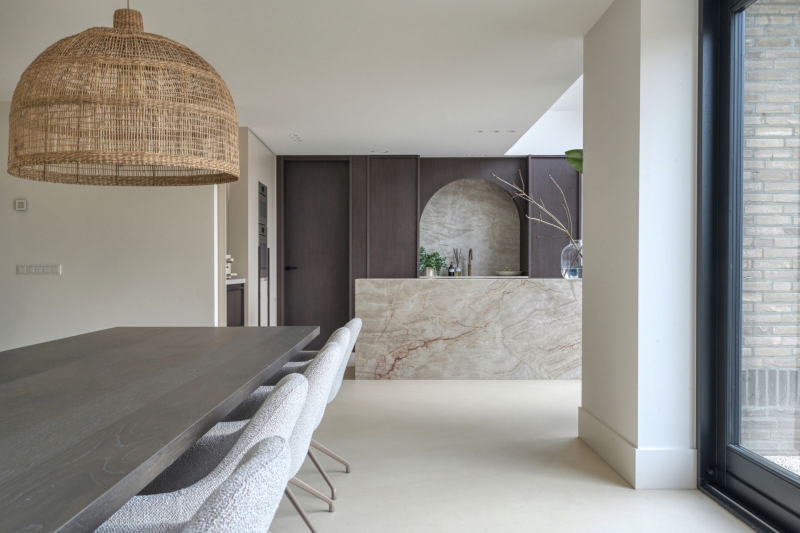 Eetkamer met een egale, crèmekleurige Pava kwartsiet gietvloer, donkere eettafel, bouclé stoelen en een kookeiland van natuursteen