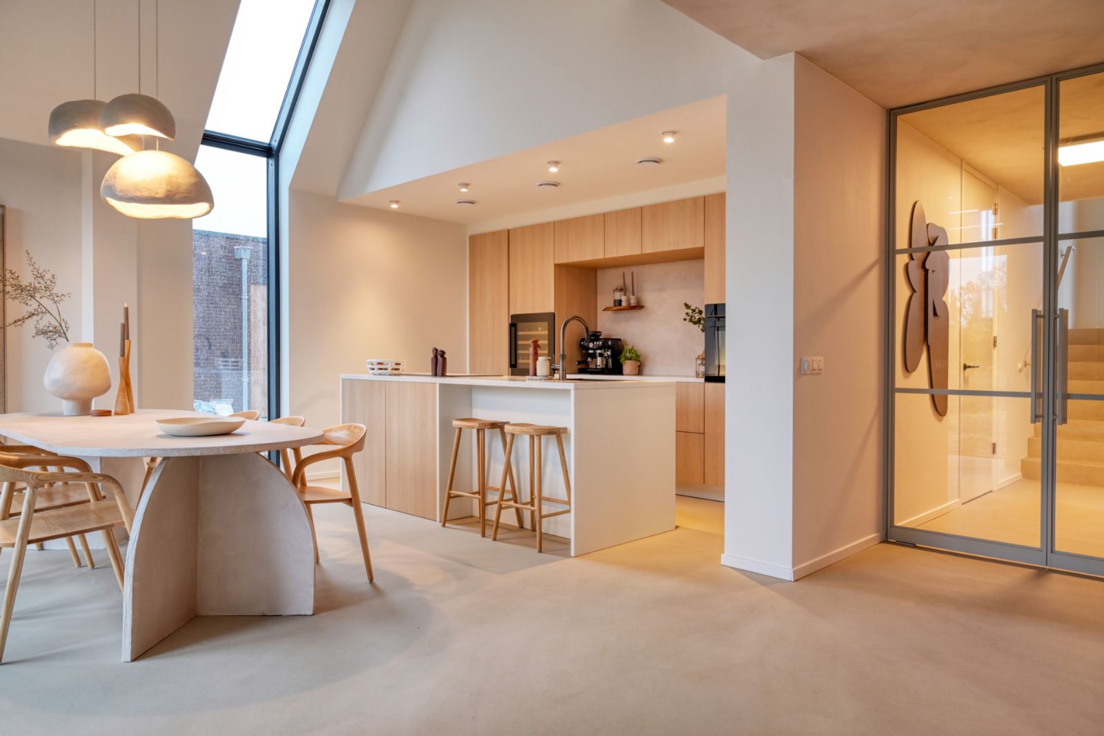 Keuken met lichte houten kastjes, eiland met barkrukken en een zandkleurige Pava lavasteen gietvloer