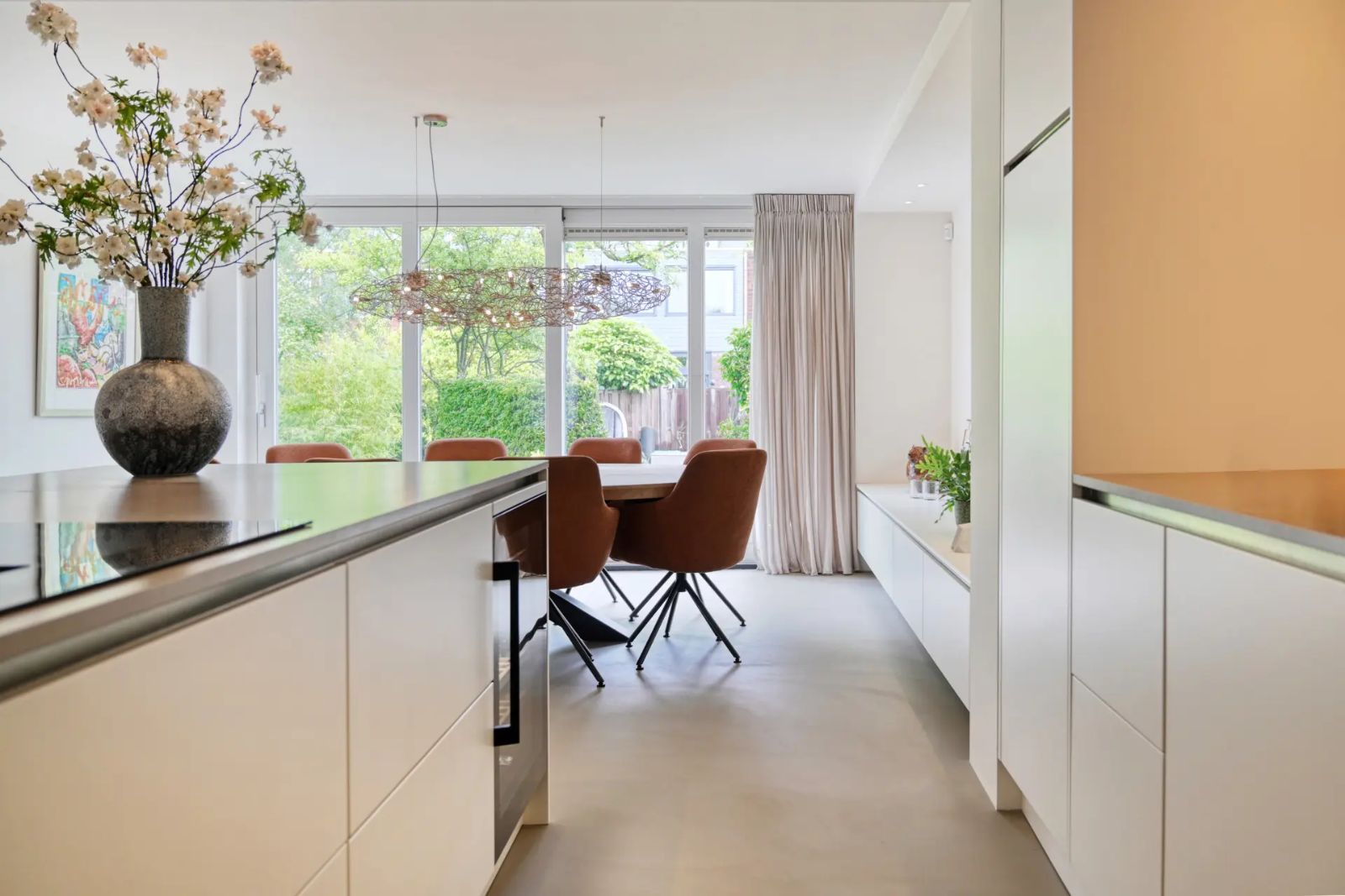 Open keuken en eethoek met een lichte Pava lavasteen gietvloer, cognackleurige stoelen en grote raampartij naar de tuin